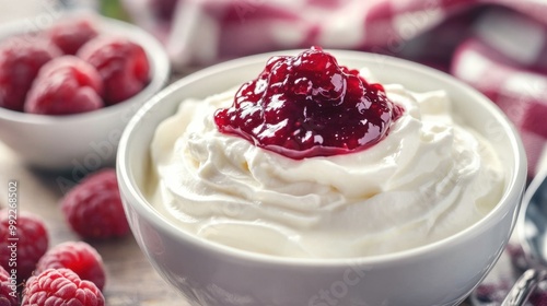 A bowl of plain yoghurt with a dollop of raspberry jam on top, ready to be mixed, on a breakfast table.