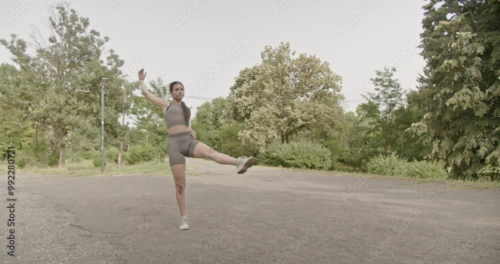 A young woman wearing fitness attire dances in an empty park. She performs a graceful, athletic routine. A young woman wearing fitness attire dances in an empty park. She performs a graceful, athletic routine.
