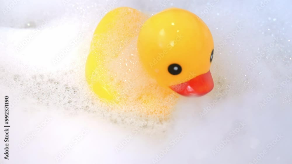 Close-up of plastic yellow toy duck swims in bathtub in the foam, sways on the surface of water, bends down with its beak Baby bathing, children's hygiene, fun leisure time, soap, tear-free shampoos Close-up of plastic yellow toy duck swims in bathtub in the foam, sways on the surface of water, bends down with its beak Baby bathing, children's hygiene, fun leisure time, soap, tear-free shampoos
