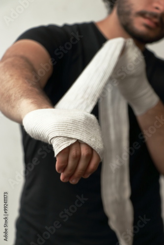Billede på lærred A man is carefully wrapping his hands with white bandages before a workout or boxing session