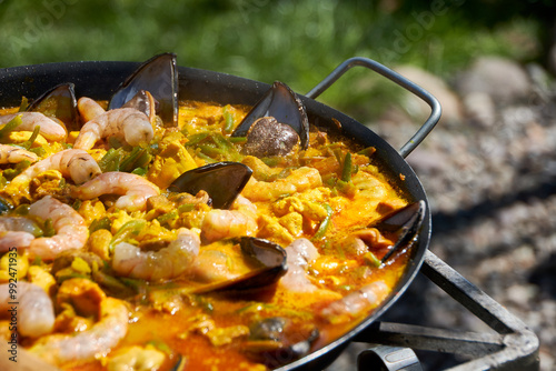 Close up while cooking a paella with vegetables, pork and seafood outdoors