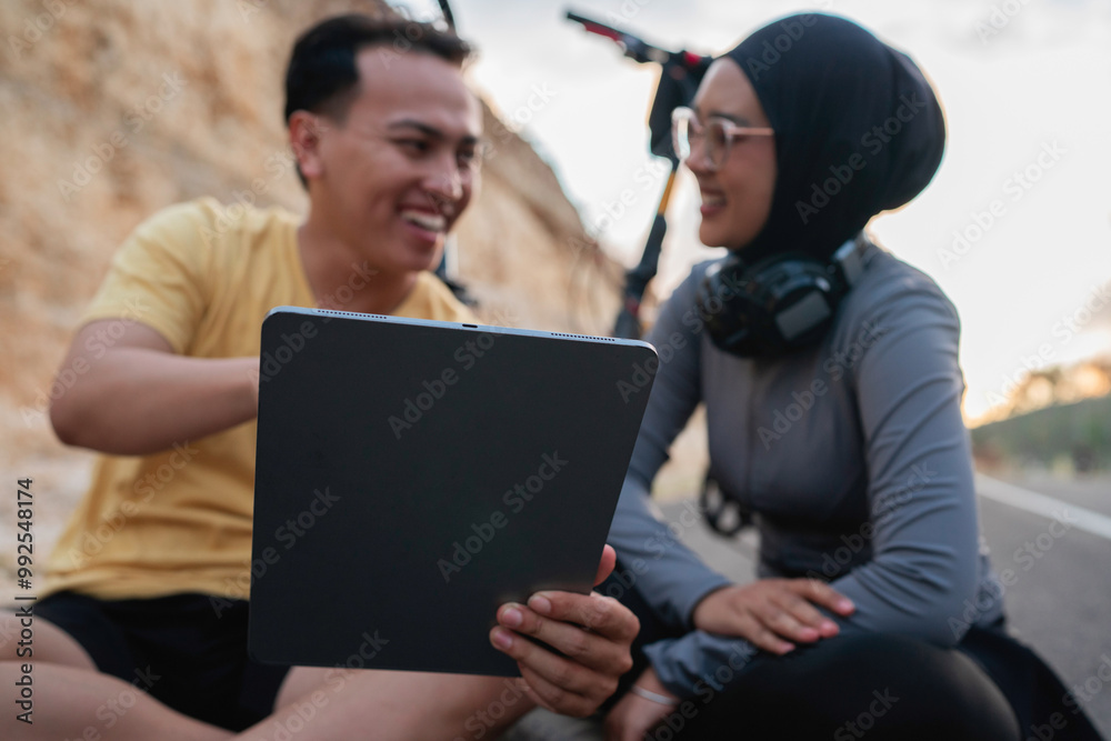 athletic bicycle rider couple using tablet, taking rest from biking athletic bicycle rider couple using tablet, taking rest from biking