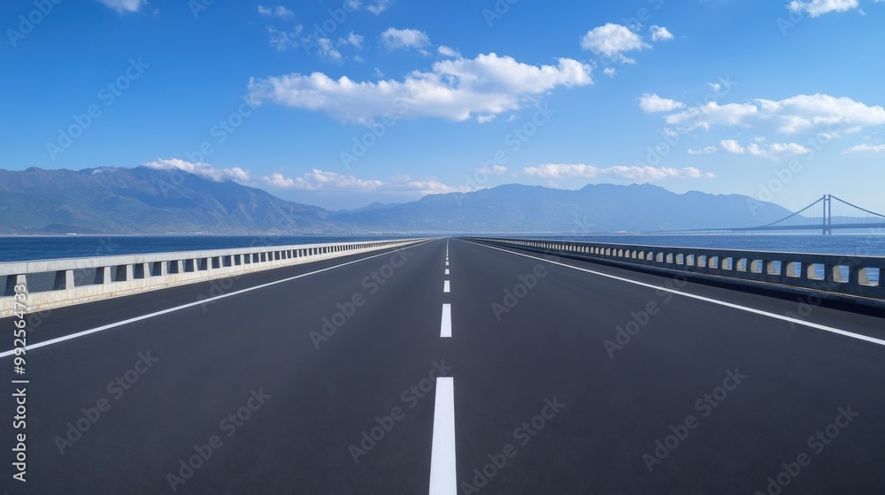 A scenic road stretches towards the horizon, framed by mountains and a serene waterfront under a clear blue sky. A scenic road stretches towards the horizon, framed by mountains and a serene waterfront under a clear blue sky.