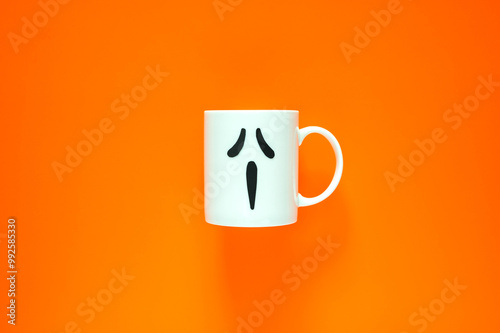 Halloween background with a coffee cup with eye and mouth stickers puts on orange background. Minimal concept. photo