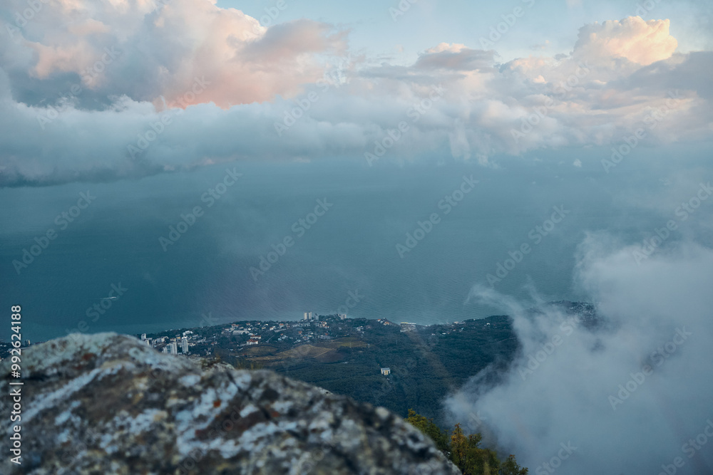 Majestic panoramic view of ocean and clouds from mountain top with person sitting on rock, contemplating nature and travel experience Majestic panoramic view of ocean and clouds from mountain top with person sitting on rock, contemplating nature and travel experience