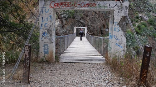 Man walks across pedestrian footbridge over rocky river canyon in Peru photo