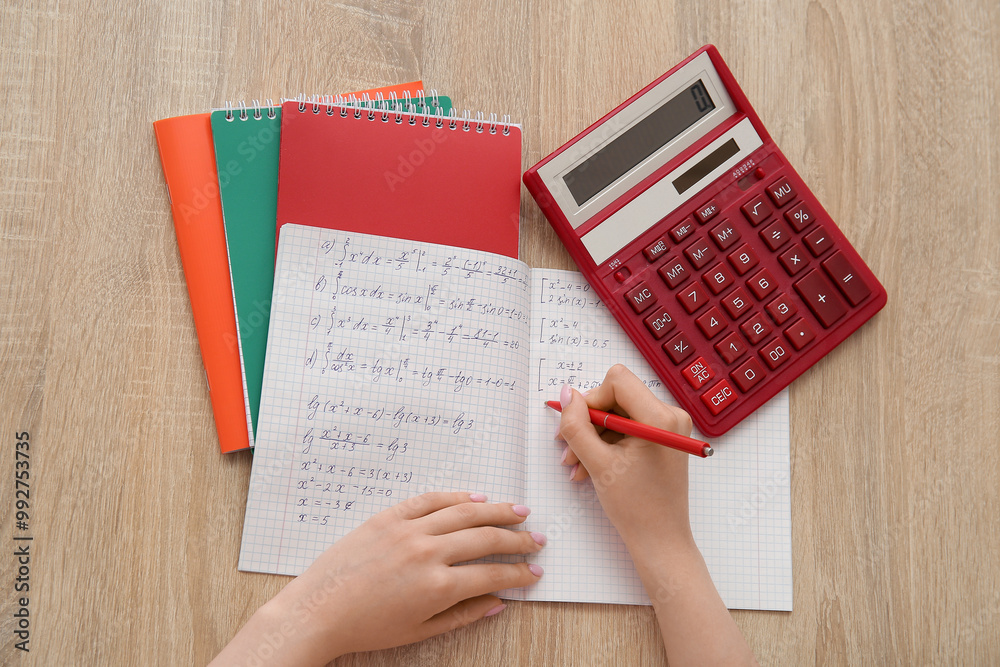 Fototapeta premium Woman writing math formulas in copybook on wooden table