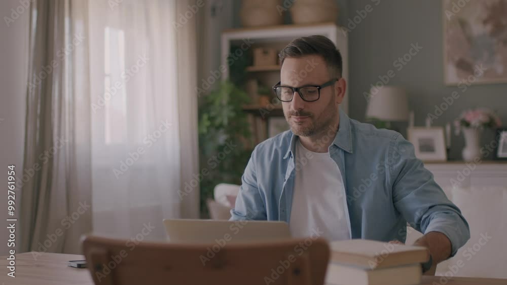 A handsome Caucasian man looking at his laptop, working online from his home and drinking a coffee. 4k video