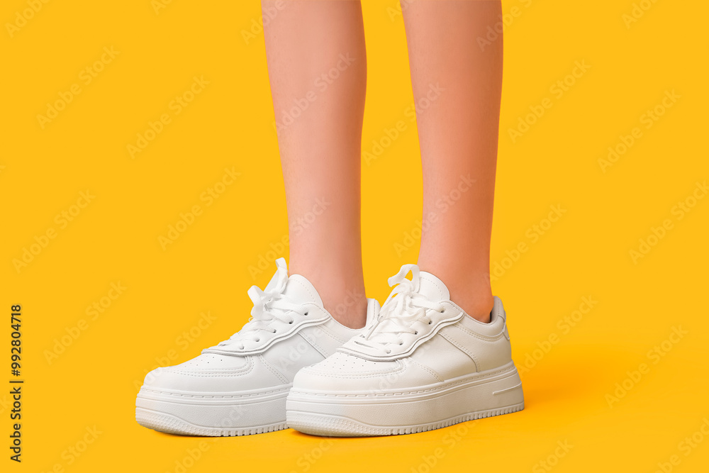 Legs of young woman in stylish white sneakers on yellow background Legs of young woman in stylish white sneakers on yellow background