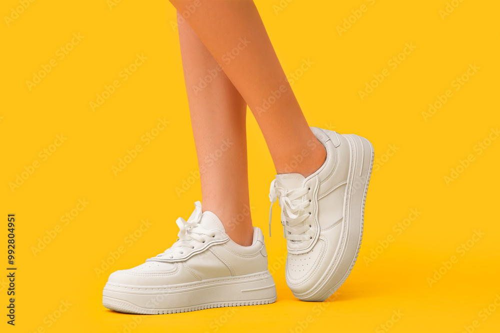 Legs of young woman in stylish white sneakers on yellow background Legs of young woman in stylish white sneakers on yellow background
