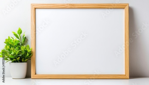 A minimalist wooden frame with a blank canvas, paired with a small green plant in a pot, perfect for decoration or design.