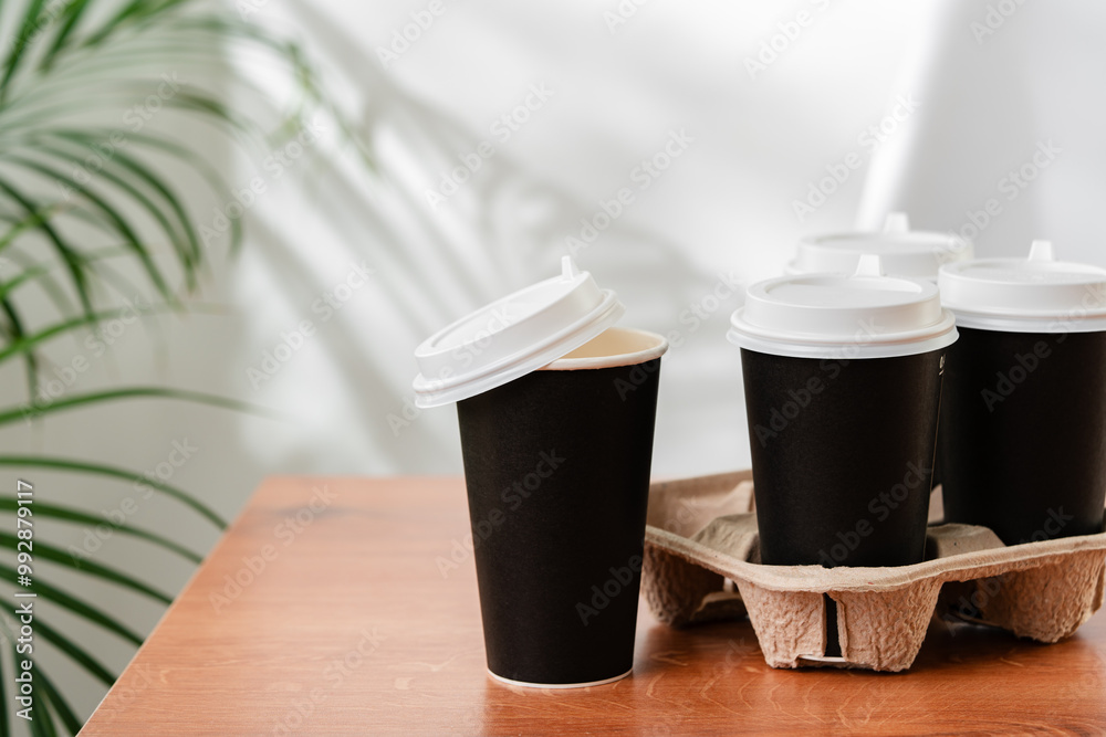 Takeout coffee cups placed on a wooden table next to a green indoor plant Takeout coffee cups placed on a wooden table next to a green indoor plant