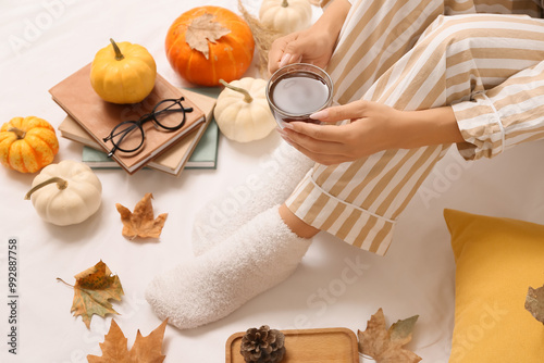 Female legs in warm socks with autumn leaves, books, cup of coffee and pumpkins on bed