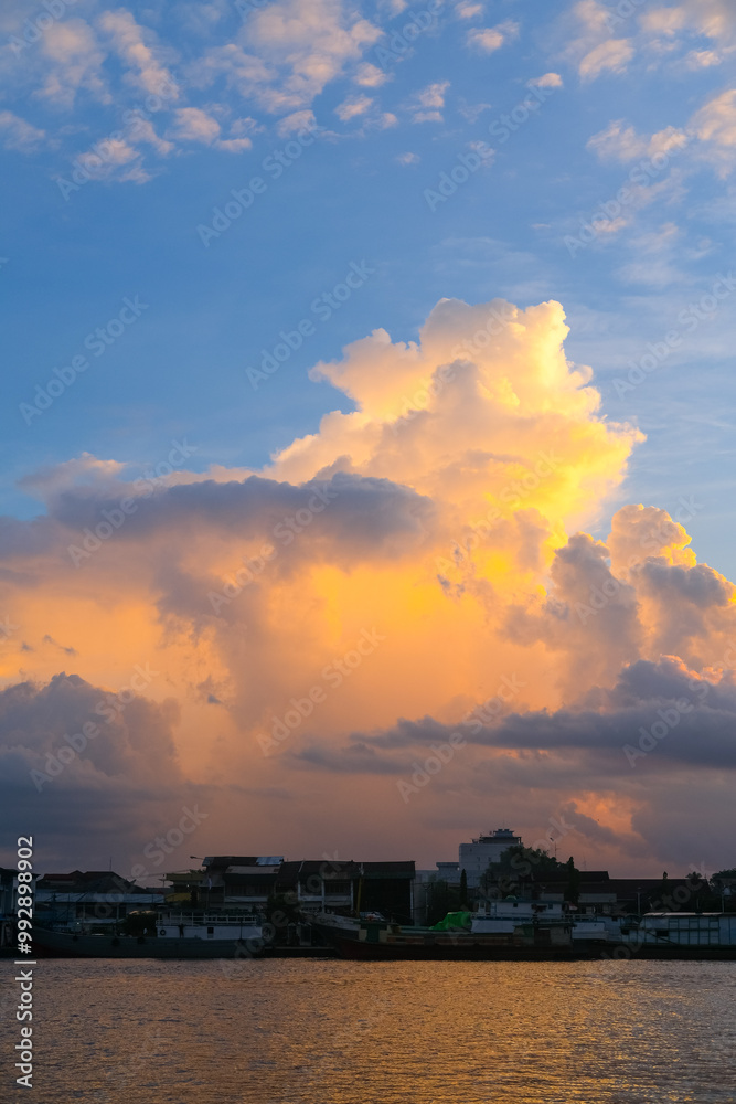 Sunset over Pontianak cityscape at Kapuas River’s edge, with vibrant blue and orange clouds reflecting on the water, capturing the serene beauty of the riverside city.
