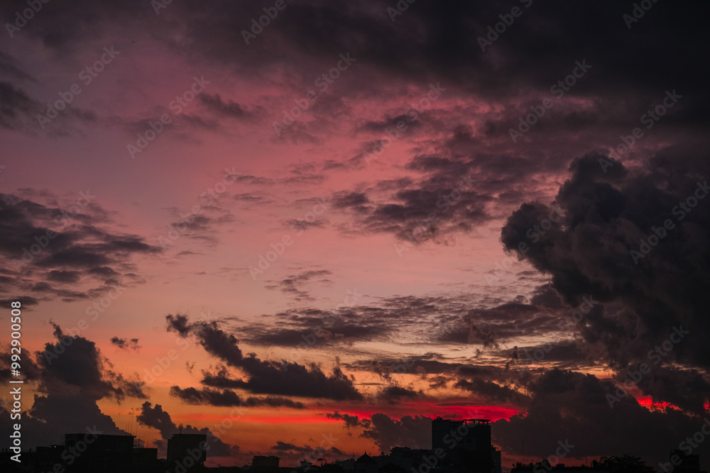 Dramatic sunset paints the sky with vibrant shades of orange, pink, and dark purple, silhouetting buildings below and creating a breathtaking evening scene full of depth and color.