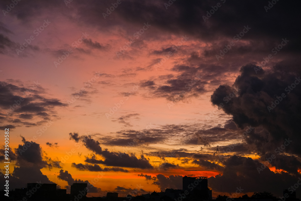 Dramatic sunset paints the sky with vibrant shades of orange, pink, and dark purple, silhouetting buildings below and creating a breathtaking evening scene full of depth and color.