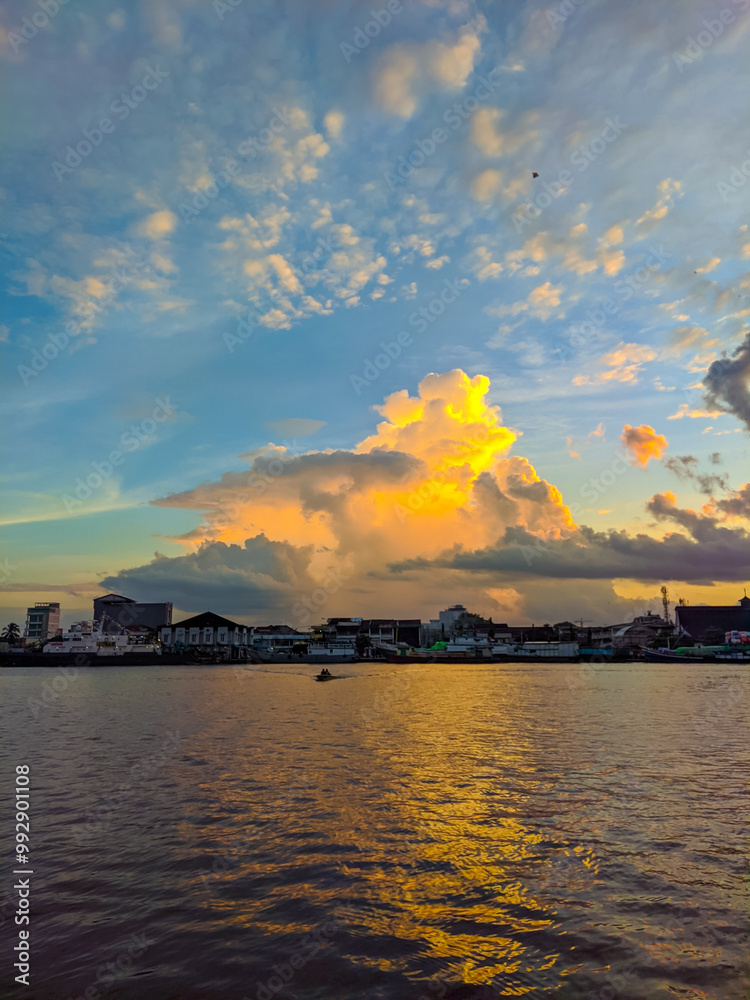Sunset over Pontianak cityscape at Kapuas River’s edge, with vibrant blue and orange clouds reflecting on the water, capturing the serene beauty of the riverside city.