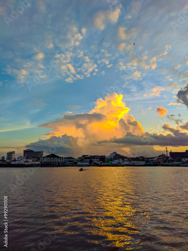 Obraz na płótnie Sunset over Pontianak cityscape at Kapuas River’s edge, with vibrant blue and orange clouds reflecting on the water, capturing the serene beauty of the riverside city. w salonie