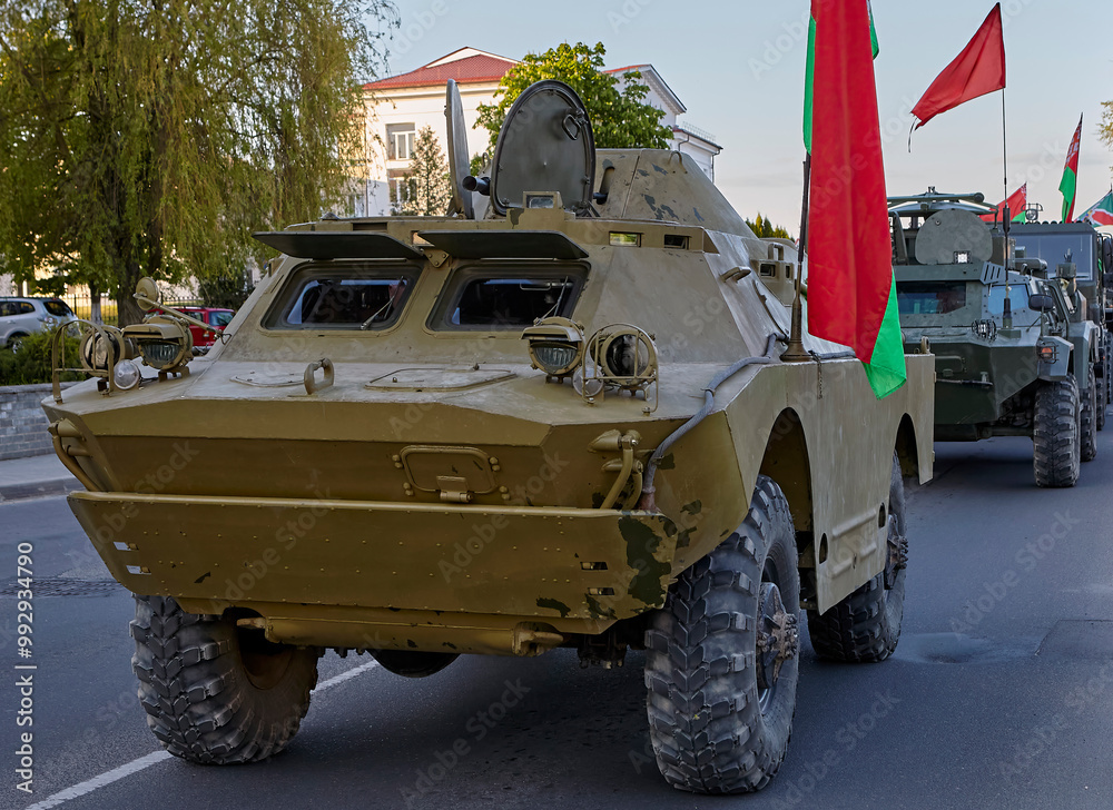 Fototapeta premium Military vehicles driving down a city street during a parade with flags displayed