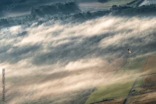 A little paraglider among low clouds over the fields