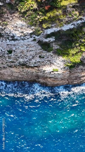 Veduta aera della roccia a picco sul mare.
Il mare verde e cristallino si infrange sulla scogliera. Video verticale photo