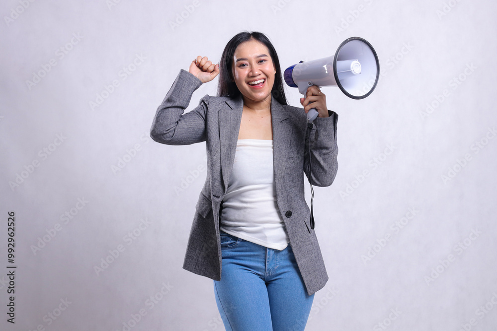 Fototapeta premium Beautiful young woman shouting formal cheerful forward hand holding megaphone loudspeaker and clenched upward wearing gray suit isolated on white background. fashion concept, lifestyle, advertising