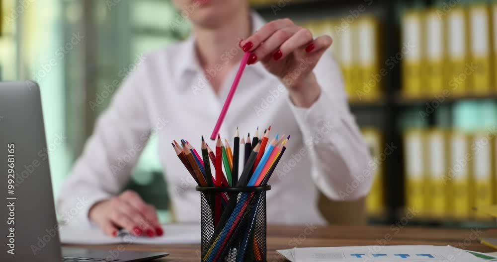 Female manager smoothly takes pink pencil out of holder with colored pencils. Senior worker makes notes on paper about mistakes in subordinate report