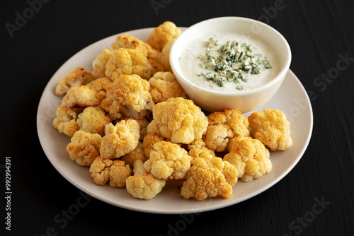 Homemade Buffalo Cauliflower with Blue Cheese Sauce on a Plate on a Black Background, side view.