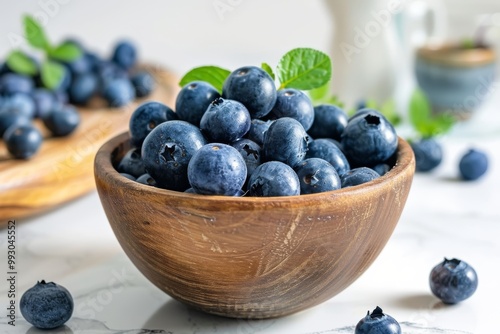 Fresh blueberries in a wooden bowl with green leaves arranged on a marble surface