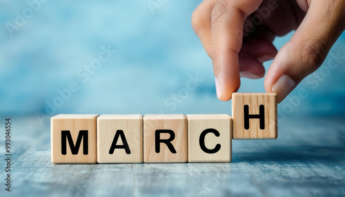 A hand is holding a block of wood with the letters MARCH