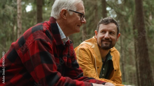 Adult son and elderly father walk together on pathway in forest, enjoying talking. Adult man supports senior people chatting and strolling. Intergenerational relationships and care for older people.