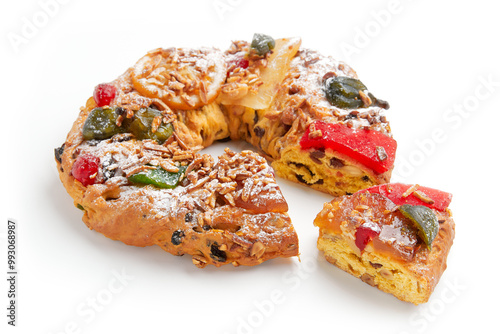 A partially sliced wreath shaped cake decorated with candied fruit, nuts, and powdered sugar