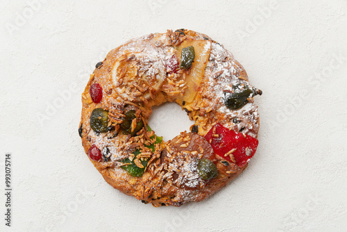 A top down view of a festive wreath shaped cake decorated with candied fruit and nuts on a white plate