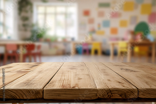 A close-up view of a wooden table with a blurred classroom background featuring colorful chairs and educational decor