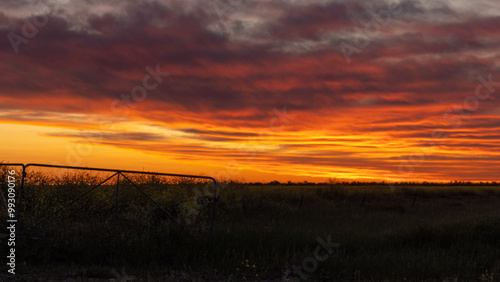 An orange sunset above a silhouetted farm gate