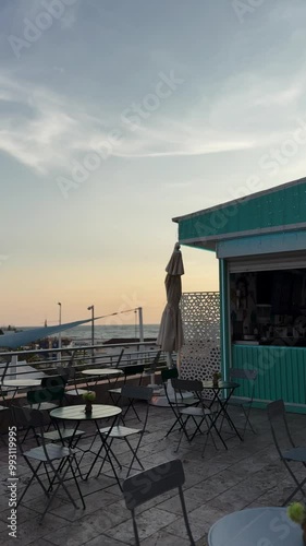 Empty outdoor seating area of a rooftop cafe overlooking the sea at sunset, with umbrellas and a pastel-colored structure. Marbella, Spain, Andalucia low season