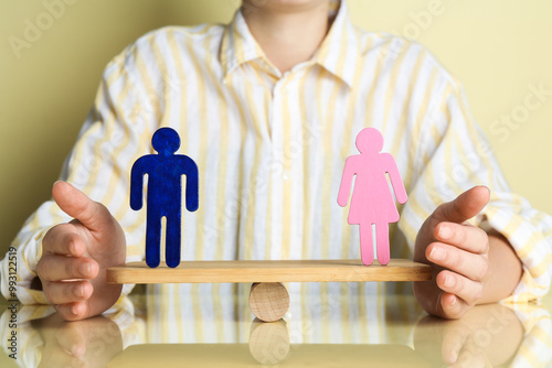 Gender equality concept. Woman with male and female figures on scales against light yellow background, closeup photo