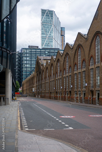 A row of classic brick industrial buildings with repetitive arched windows contrasts with a modern glass-cased tower in the background, showcasing historical and contemporary elements in London