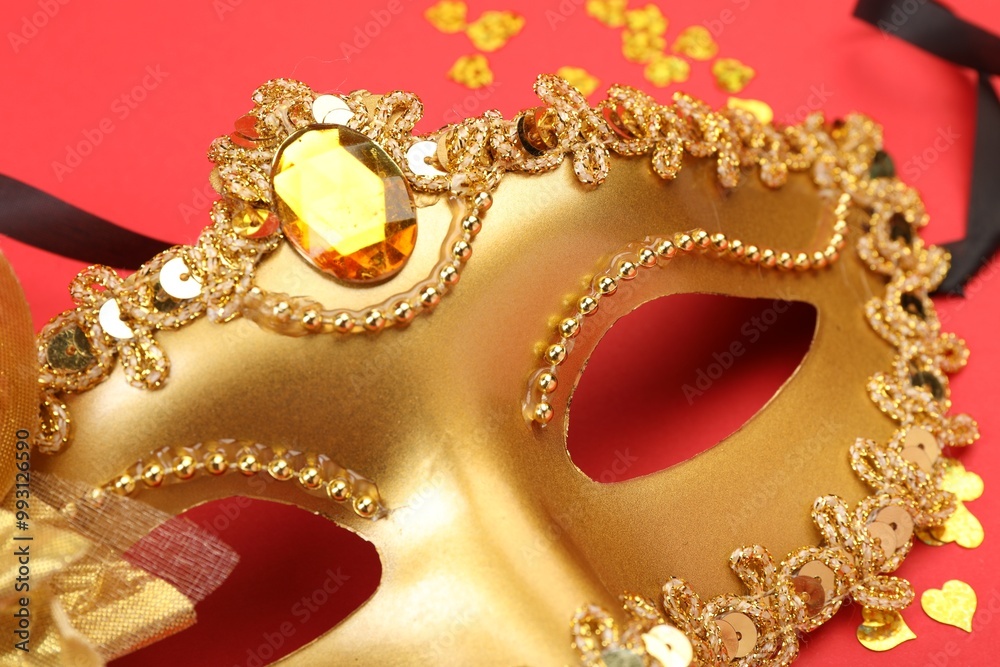 One golden carnival mask and confetti on red background, closeup One golden carnival mask and confetti on red background, closeup