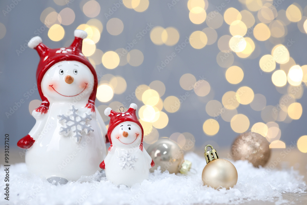 Funny snowmen figure and Christmas balls on artificial snow against blurred lights Funny snowmen figure and Christmas balls on artificial snow against blurred lights