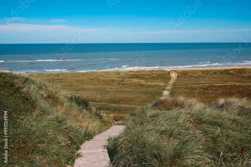 Danish Coastal Landscape. Hilly coast of the northern sea. Sun, blue sky, clouds, waves and grass. Beautiful landscape summer on the northern sea