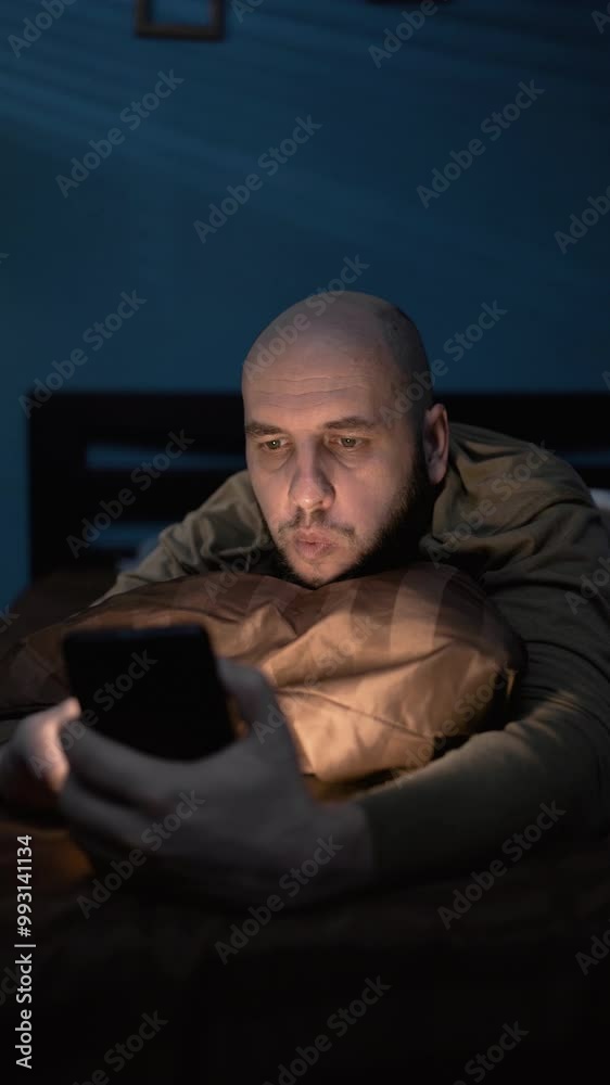 Millennial man with smartphone lying in bed at home at night. Millennial man with smartphone lying in bed at home at night.