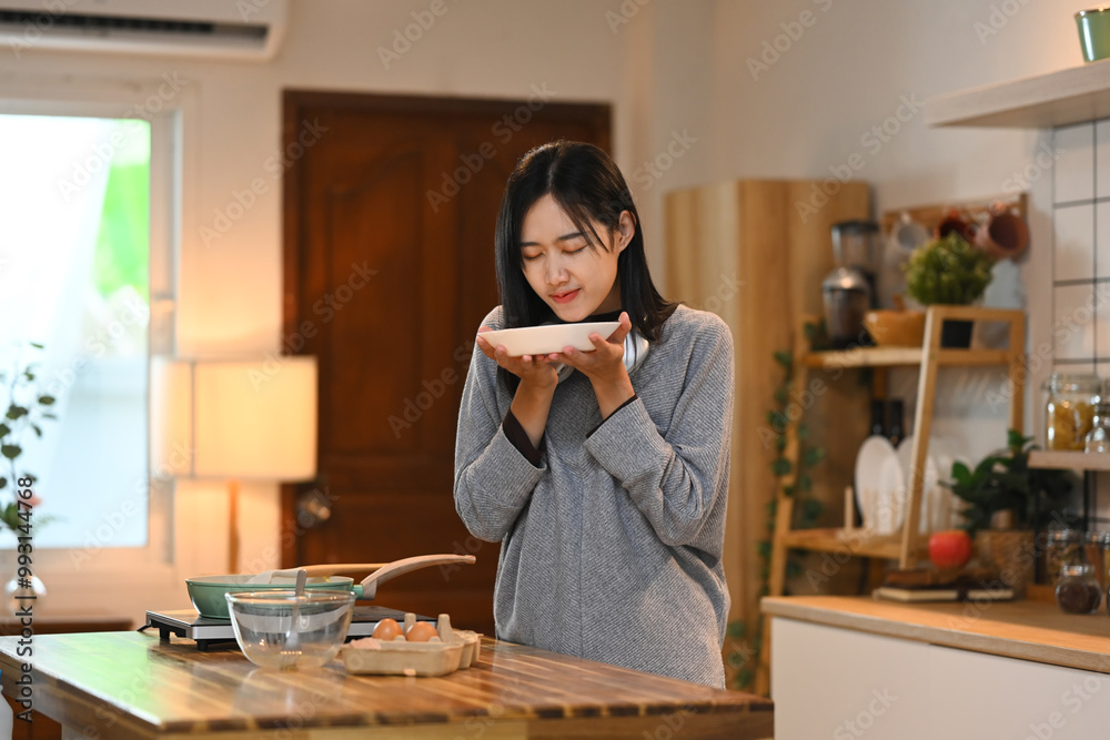 Young woman standing in the kitchen and smelling fresh healthy breakfast in plate Young woman standing in the kitchen and smelling fresh healthy breakfast in plate