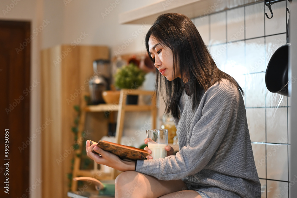 Peaceful young asian woman sitting at kitchen table and reading book Peaceful young asian woman sitting at kitchen table and reading book