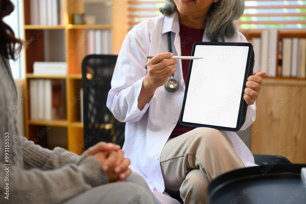 Senior female doctor holding digital tablet discussing with patient in medical office Senior female doctor holding digital tablet discussing with patient in medical office