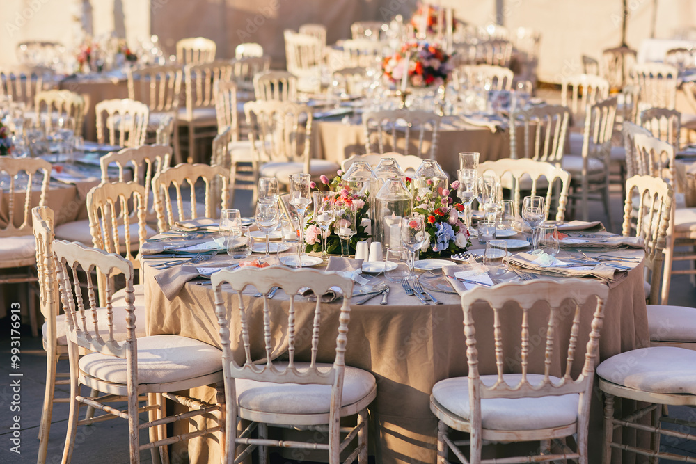 Elegant Outdoor Wedding Reception with Draped Canopy, Floral Centerpieces, and White Chairs Overlooking a Waterfront Venue Elegant Outdoor Wedding Reception with Draped Canopy, Floral Centerpieces, and White Chairs Overlooking a Waterfront Venue