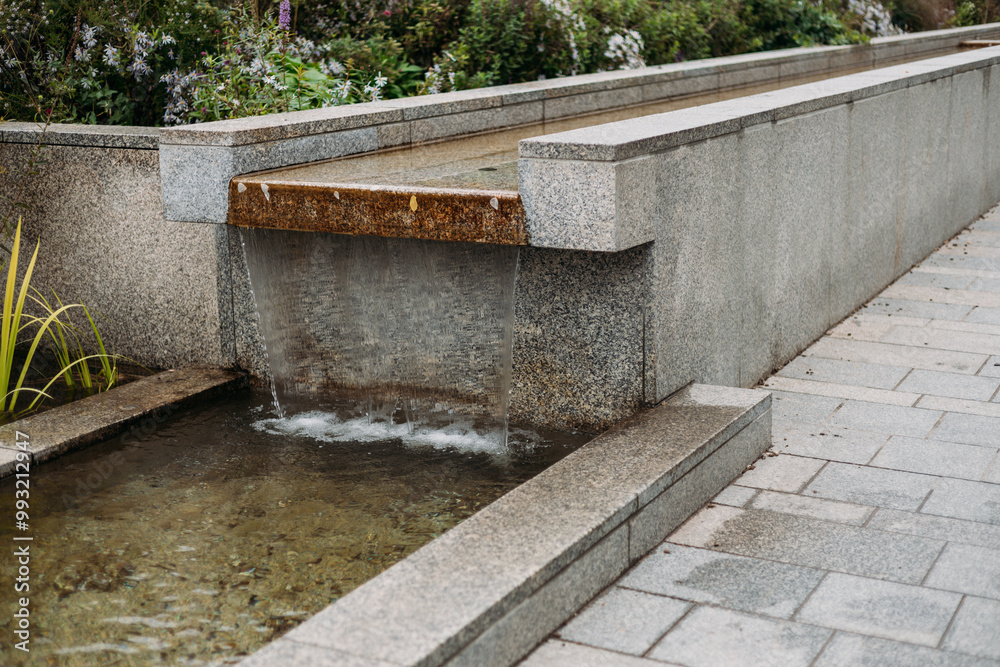 Modern water fall in the city park. Water flows over the stone slabs of the city fountain. Elements of architectural decorations Modern water fall in the city park. Water flows over the stone slabs of the city fountain. Elements of architectural decorations