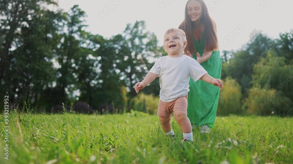 Mom and baby taking the first steps. Happy family kid dream concept. A baby is walking on the grass in a park. Mom and baby walking on grass on first steps in the lifestyle park. Mom and baby taking the first steps. Happy family kid dream concept. A baby is walking on the grass in a park. Mom and baby walking on grass on first steps in the lifestyle park.