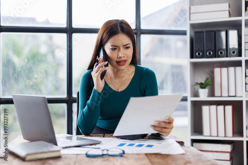 Asian woman entrepreneur busy with her work in the office. Young Asian woman work on desk laptop phone while planning sales, research or financial strategy in company 