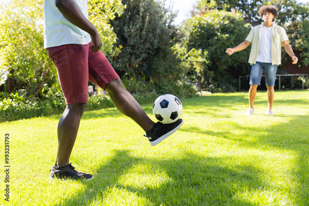 Playing soccer in backyard, two diverse male friends enjoying outdoor activity together